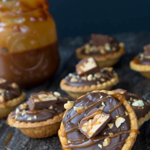 Mini Salted Caramel Snickers Tarts! Mini pre-baked tart shells with a salted caramel peanut filling and a chocolate peanut butter topping. Finish it off with chopped snickers and more peanuts, and you have the easiest/most decadent and delicious, bite-sized dessert!