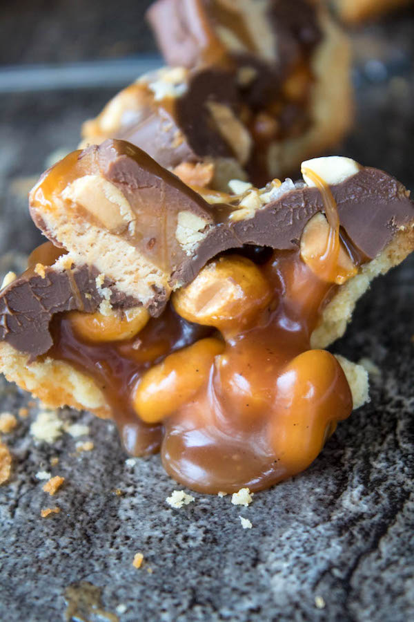 Mini Salted Caramel Snickers Tarts! Mini pre-baked tart shells with a salted caramel peanut filling and a chocolate peanut butter topping. Finish it off with chopped snickers and more peanuts, and you have the easiest/most decadent and delicious, bite-sized dessert!