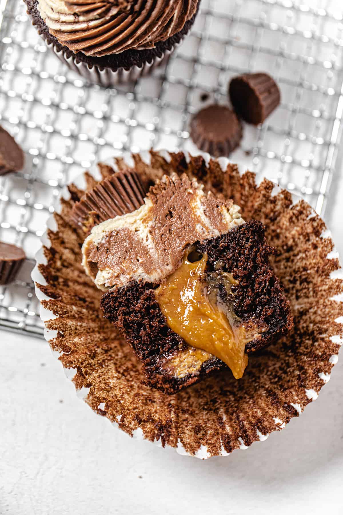 halved peanut butter filled cupcake on a cupcake liner with mini chocolate peanut butter cups around it