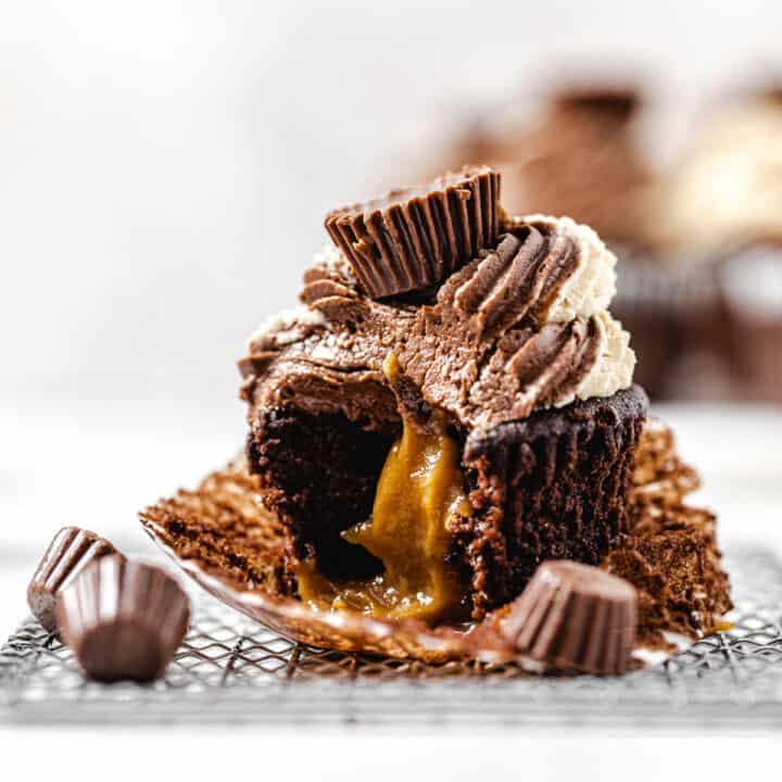 peanut butter filled cupcake with a bite taken out of it on a small wire rack with mini peanut butter cups around it