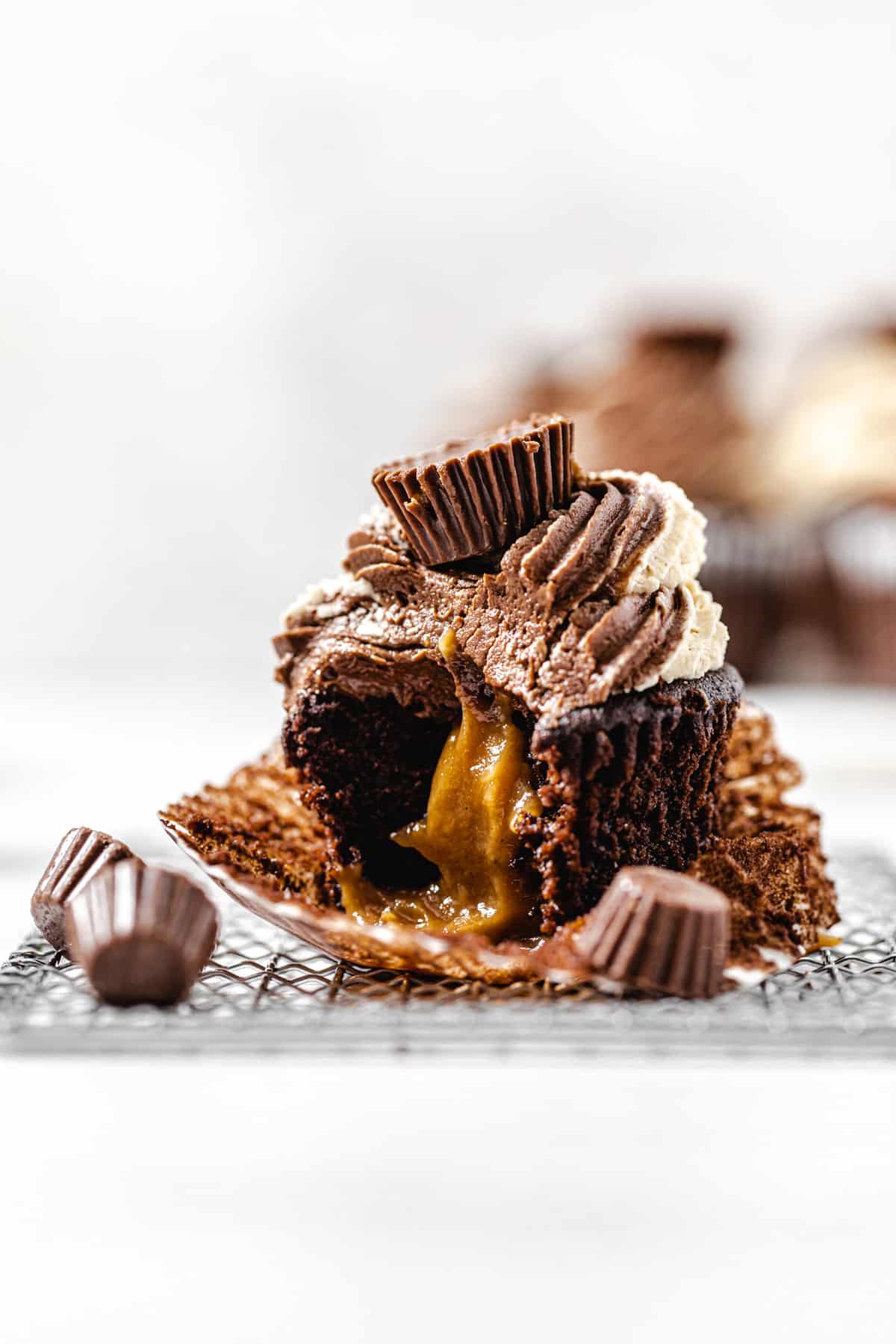 peanut butter filled cupcake with a bite taken out of it on a small wire rack with mini peanut butter cups around it