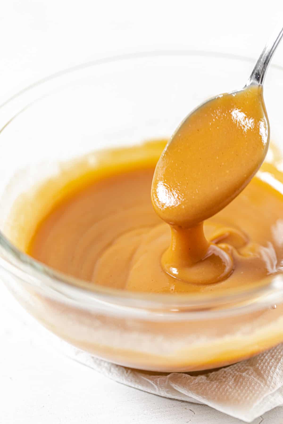 peanut butter ganache spilling off a spoon into a glass bowl