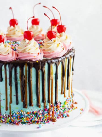 chocolate cake filled with vanilla sprinkle, caramel and chocolate buttercream and covered in a teal sprinkle frosting, topped with maraschino cherries and decorated with more sprinkles.