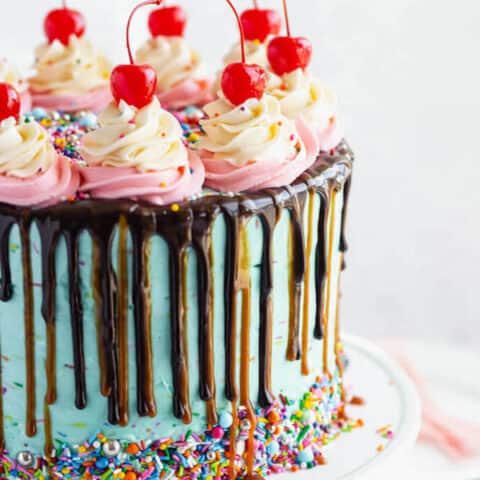 chocolate cake filled with vanilla sprinkle, caramel and chocolate buttercream and covered in a teal sprinkle frosting, topped with maraschino cherries and decorated with more sprinkles.