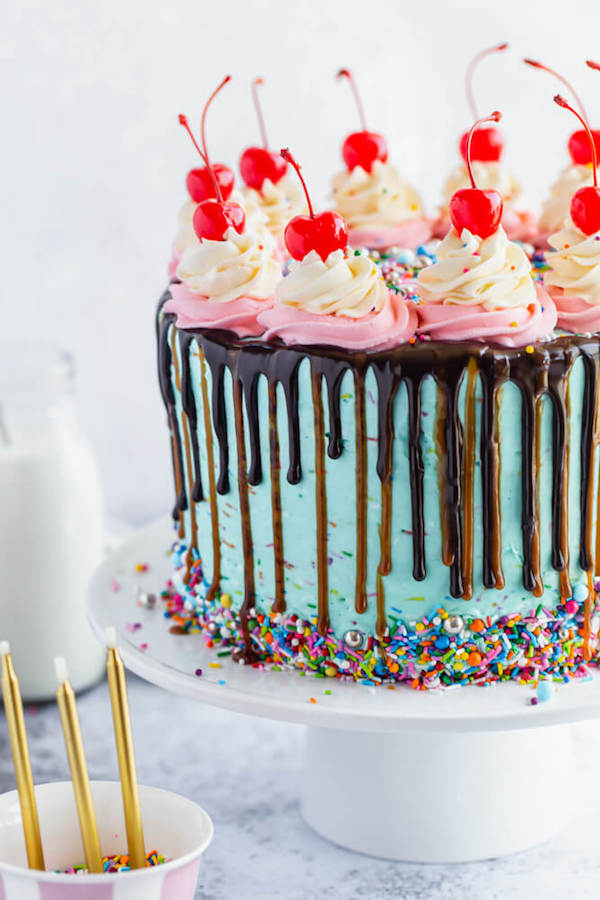 chocolate cake filled with vanilla sprinkle, caramel and chocolate buttercream and covered in a teal sprinkle frosting, topped with maraschino cherries and decorated with more sprinkles.