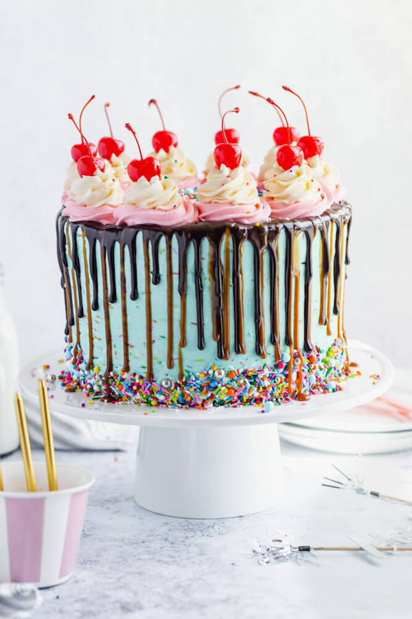 chocolate cake filled with vanilla sprinkle, caramel and chocolate buttercream and covered in a teal sprinkle frosting, topped with maraschino cherries and decorated with more sprinkles.