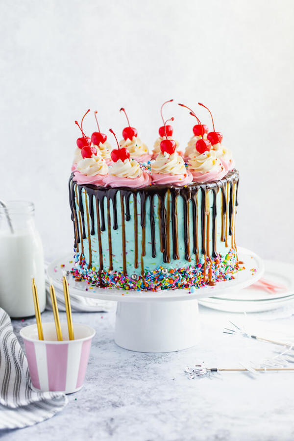 chocolate cake filled with vanilla sprinkle, caramel and chocolate buttercream and covered in a teal sprinkle frosting, topped with maraschino cherries and decorated with more sprinkles.