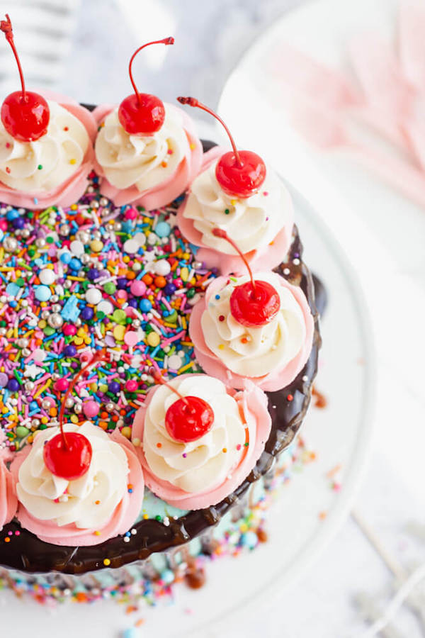 chocolate cake filled with vanilla sprinkle, caramel and chocolate buttercream and covered in a teal sprinkle frosting, topped with maraschino cherries and decorated with more sprinkles.