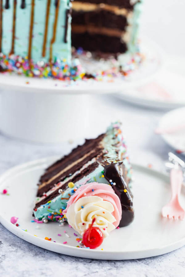 chocolate cake filled with vanilla sprinkle, caramel and chocolate buttercream and covered in a teal sprinkle frosting, topped with maraschino cherries and decorated with more sprinkles.