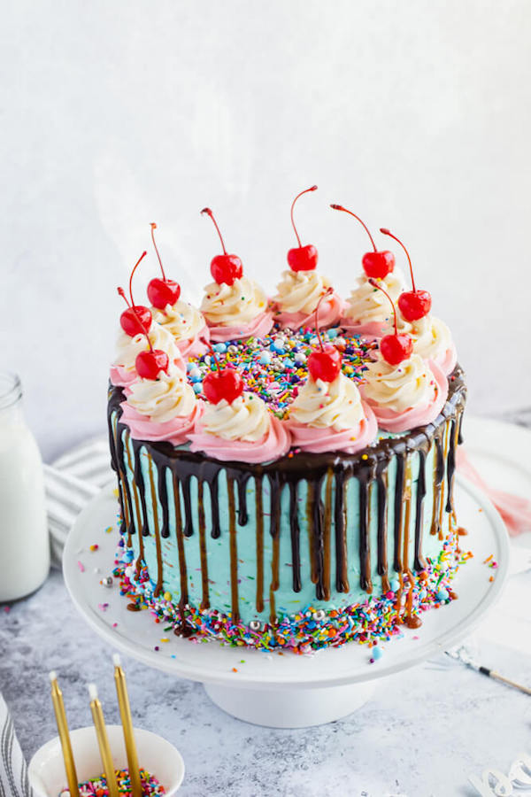 chocolate cake filled with vanilla sprinkle, caramel and chocolate buttercream and covered in a teal sprinkle frosting, topped with maraschino cherries and decorated with more sprinkles.