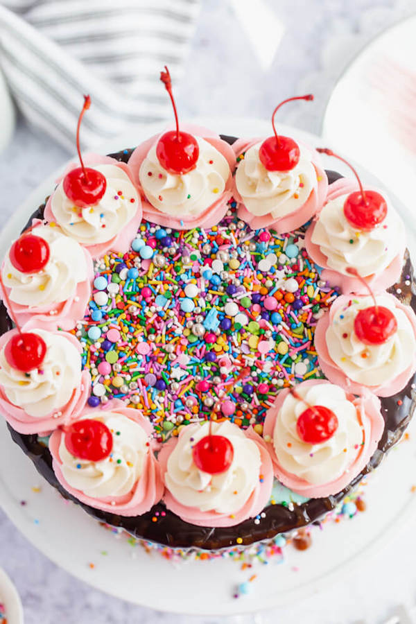 chocolate cake filled with vanilla sprinkle, caramel and chocolate buttercream and covered in a teal sprinkle frosting, topped with maraschino cherries and decorated with more sprinkles.