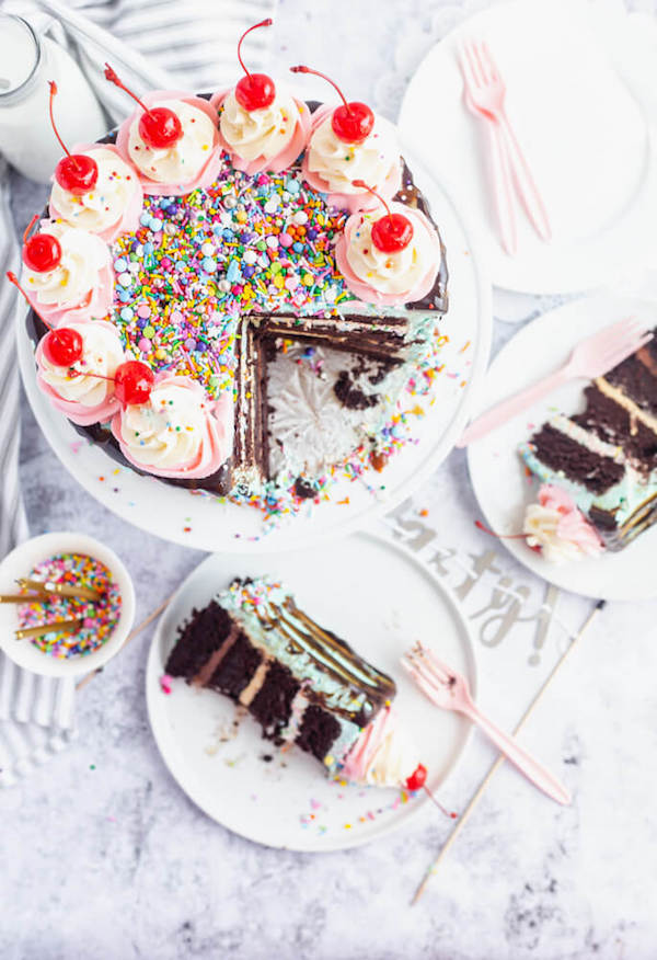 chocolate cake filled with vanilla sprinkle, caramel and chocolate buttercream and covered in a teal sprinkle frosting, topped with maraschino cherries and decorated with more sprinkles.