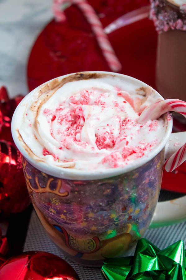 This Candy Cane Hot Chocolate is a warm and cozy Holiday drink perfect for warming up to the cold weather. With a candy cane lined rim, peppermint hot chocolate filled with crushed candy canes, and a peppermint whipped cream topping, this drink screams Christmas! 