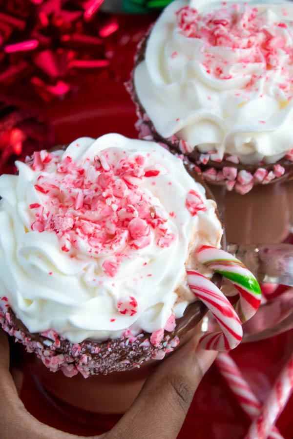 This Candy Cane Hot Chocolate is a warm and cozy Holiday drink perfect for warming up to the cold weather. With a candy cane lined rim, peppermint hot chocolate filled with crushed candy canes, and a peppermint whipped cream topping, this drink screams Christmas! 