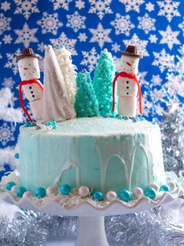 This Winter Wonderland Cake has all the magic and beauty of winter inside a cake! With a wintery white and blue theme, marshmallow snowmen, sugar cone Christmas trees and a powdered sugar snow drip, this is the perfect dessert for your Winter Wonderland themed party!