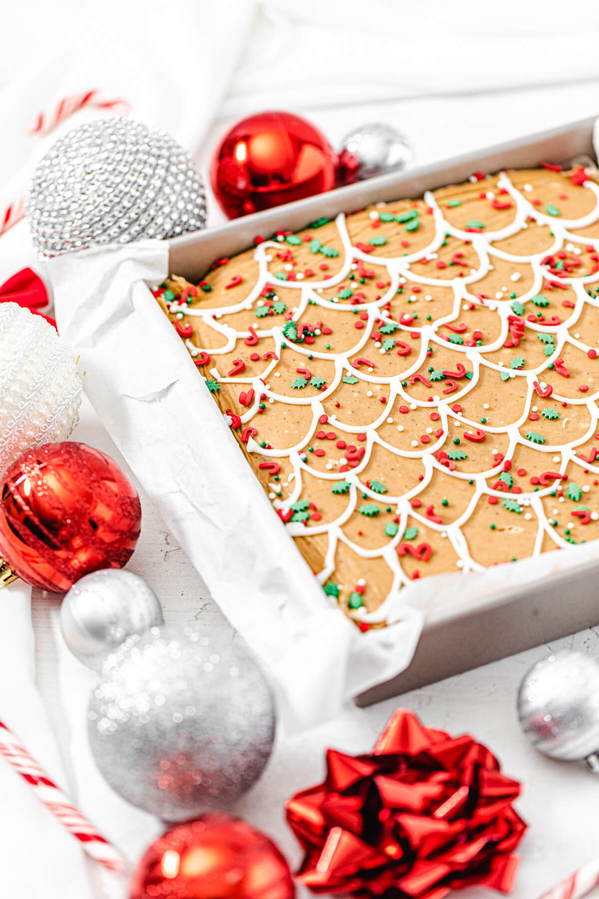 gingerbread fudge in a square pan with red and silver ornaments surrounding it