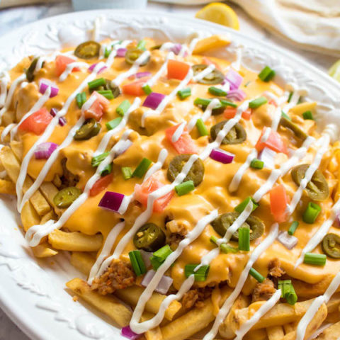 These Loaded Cheese Fries are guaranteed to be a crowd pleaser! Crisp french fries loaded with hot Italian sausage, jalapeños, red onions, green onions, tomatoes, sour cream and a creamy and delicious cheese sauce!