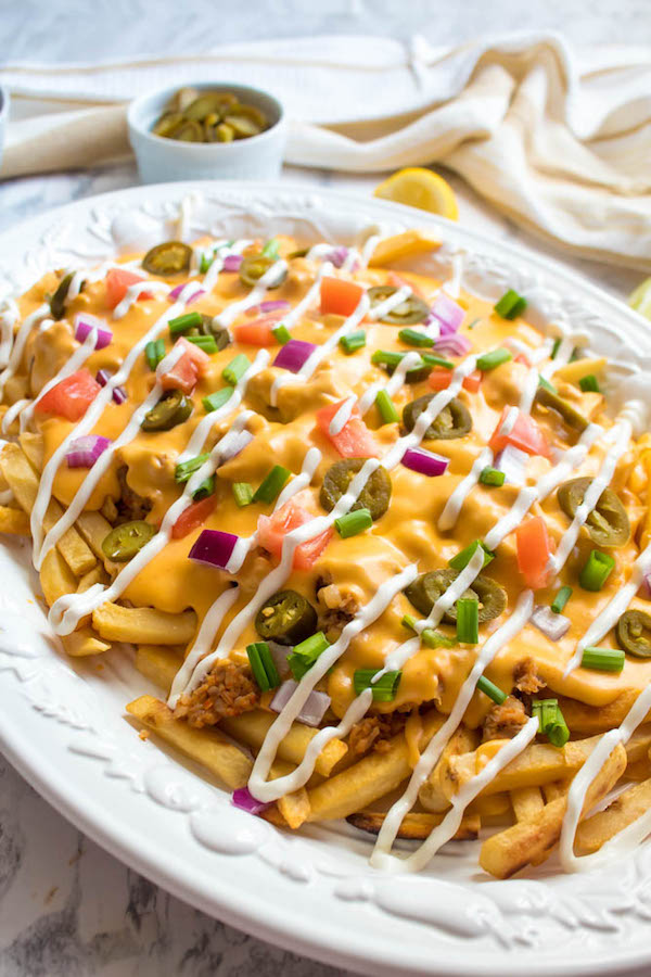 These Loaded Cheese Fries are guaranteed to be a crowd pleaser! Crisp french fries loaded with hot Italian sausage, jalapeños, red onions, green onions, tomatoes, sour cream and a creamy and delicious cheese sauce!