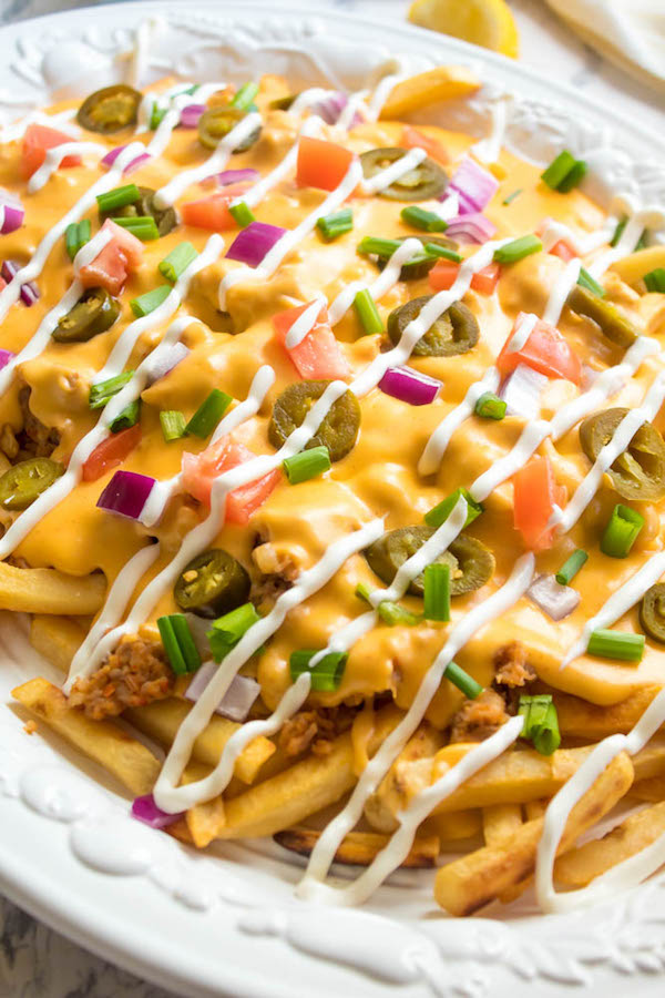 These Loaded Cheese Fries are guaranteed to be a crowd pleaser! Crisp french fries loaded with hot Italian sausage, jalapeños, red onions, green onions, tomatoes, sour cream and a creamy and delicious cheese sauce!