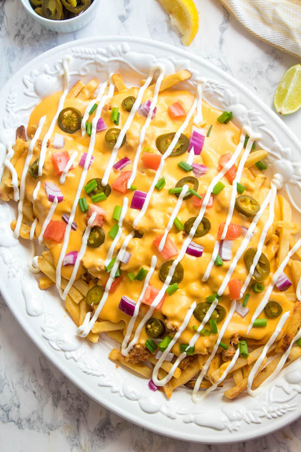 These Loaded Cheese Fries are guaranteed to be a crowd pleaser! Crisp french fries loaded with hot Italian sausage, jalapeños, red onions, green onions, tomatoes, sour cream and a creamy and delicious cheese sauce!