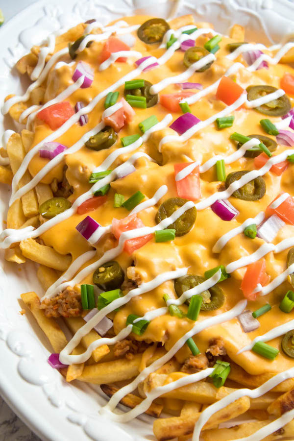 These Loaded Cheese Fries are guaranteed to be a crowd pleaser! Crisp french fries loaded with hot Italian sausage, jalapeños, red onions, green onions, tomatoes, sour cream and a creamy and delicious cheese sauce!