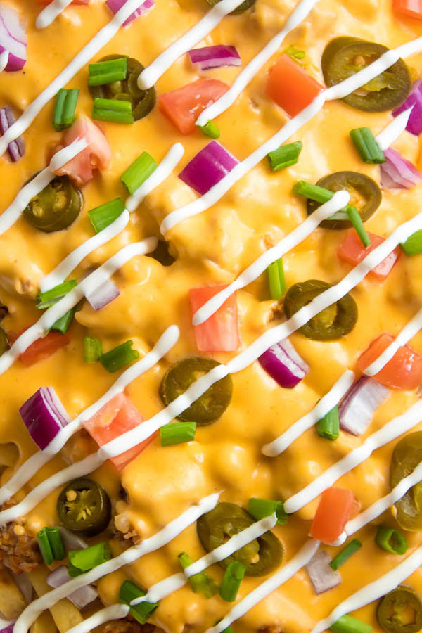 These Loaded Cheese Fries are guaranteed to be a crowd pleaser! Crisp french fries loaded with hot Italian sausage, jalapeños, red onions, green onions, tomatoes, sour cream and a creamy and delicious cheese sauce!