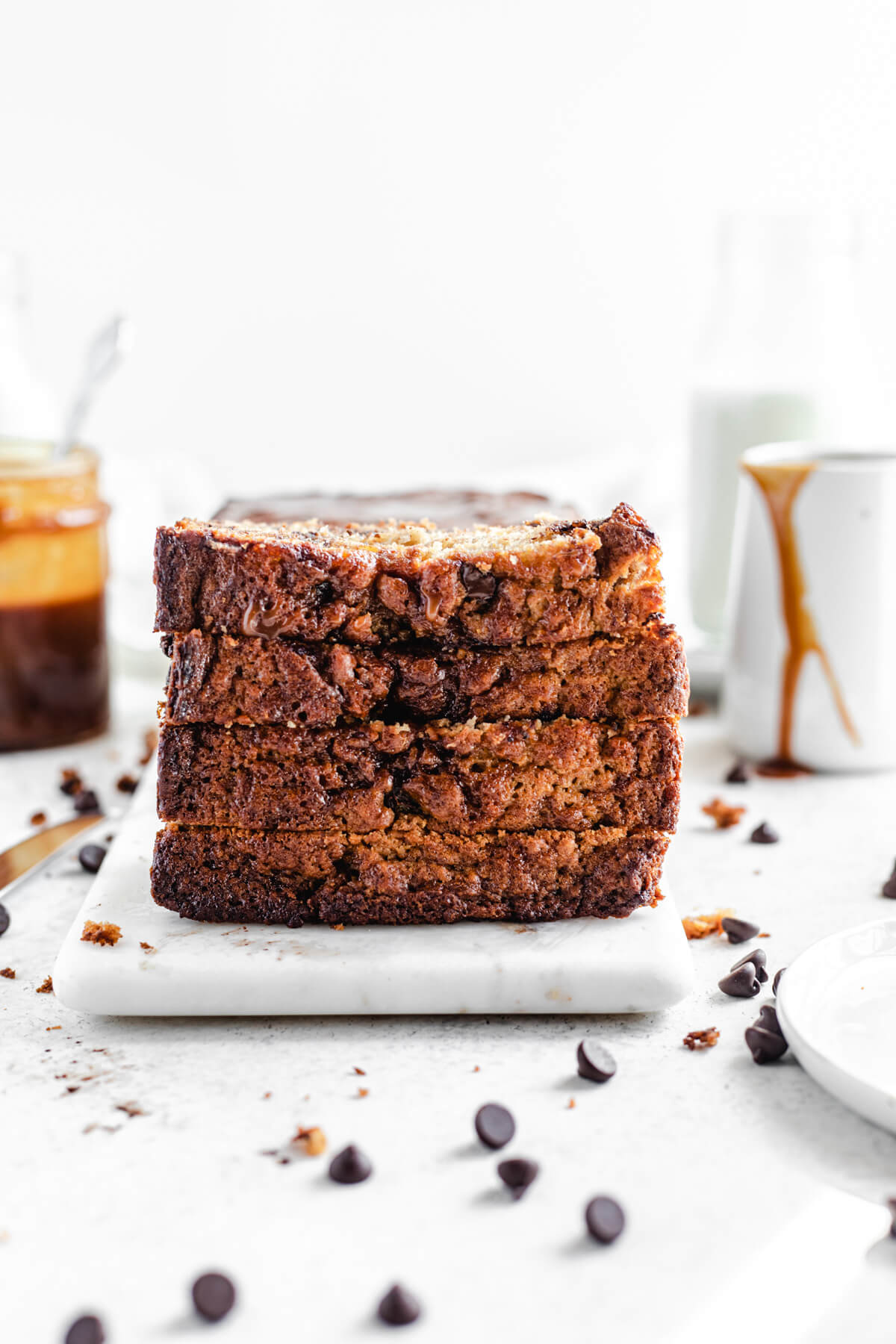 four slices of banana bread stacked on top of each other with a jar of salted caramel in the background