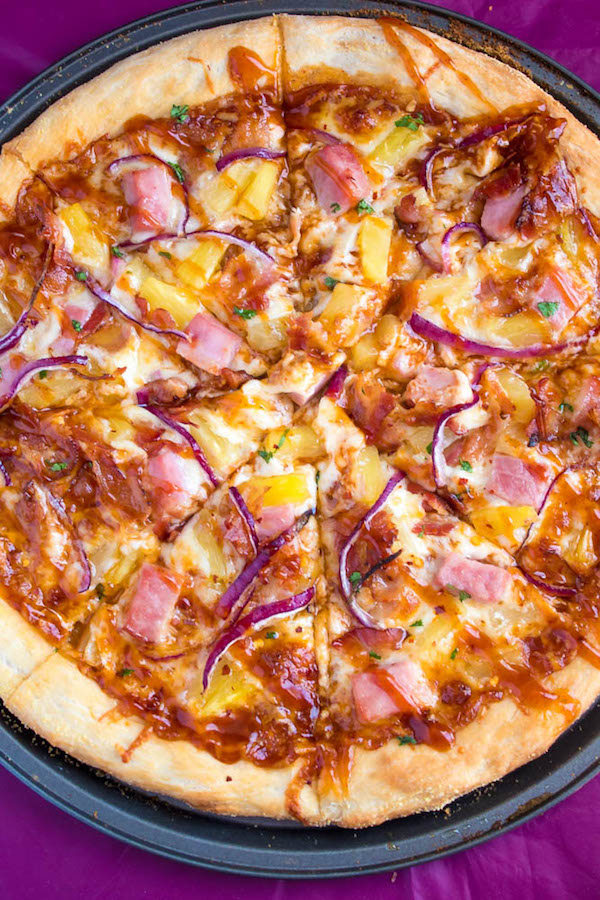 Hawaiian BBQ Pizza — Thick and chewy pizza crust topped with tangy barbecue sauce, ham, pineapple, bacon, red onions and loads of cheese. This flavourful pizza will definitely be your family's new Friday night fave!