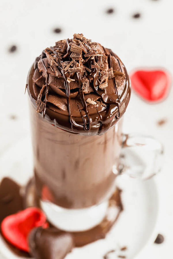 swirl of chocolate whipped cream and chocolate curls on top of a glass of ganache hot chocolate