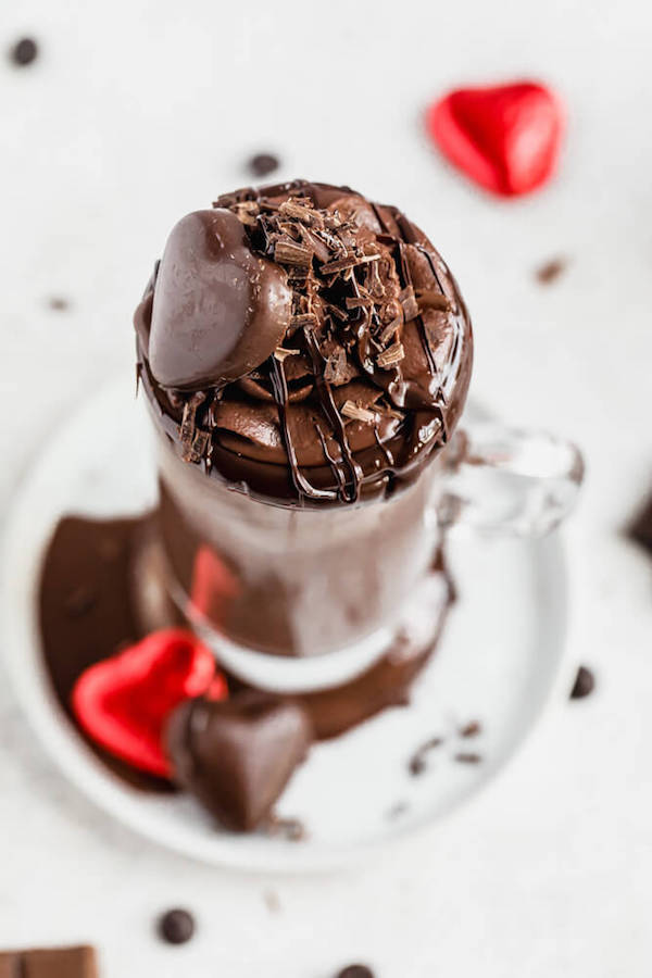 top view of hot chocolate drink topped with chocolate whipped cream, chocolate curls, melted chocolate and a chocolate heart