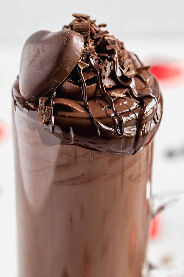 super close shot of mug of hot chocolate with chocolate on the rim and chocolate whipped cream and a chocolate heart on top