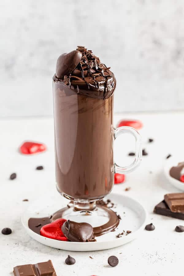 Tall glass of dark hot chocolate on a small white plate