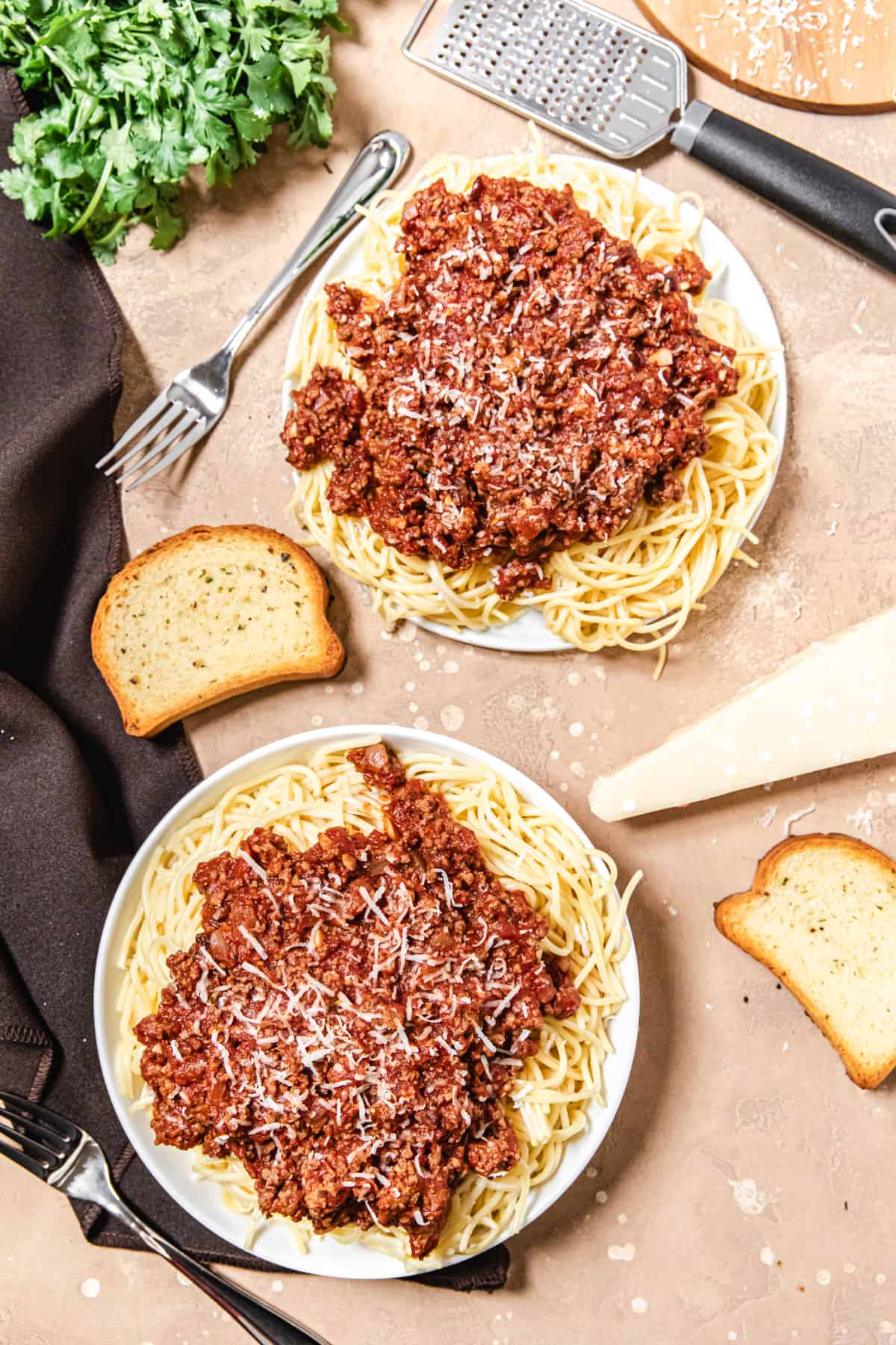two plates of spaghetti and meat sauce with garlic bread, parmesan and cilantro around them