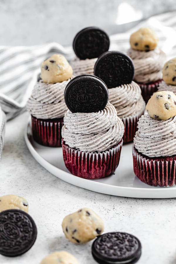 cupcakes topped with Oreos and cookie dough balls on a white plate