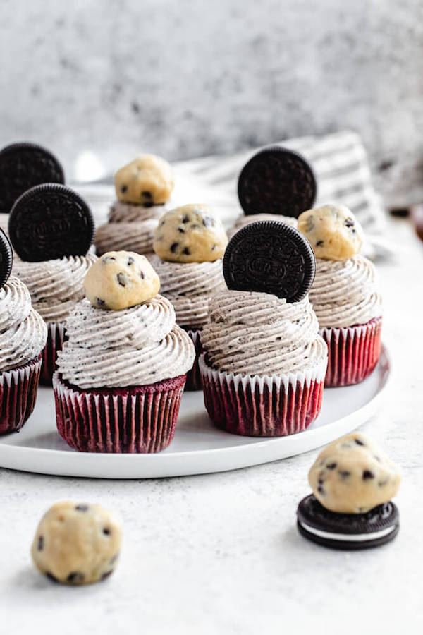 cookie dough and Oreo topped red velvet cupcakes on a white plate