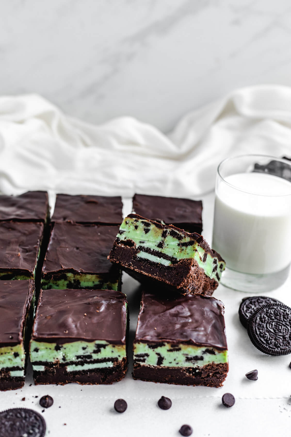 brownie leaning on other brownies with glass of milk and Oreos in background