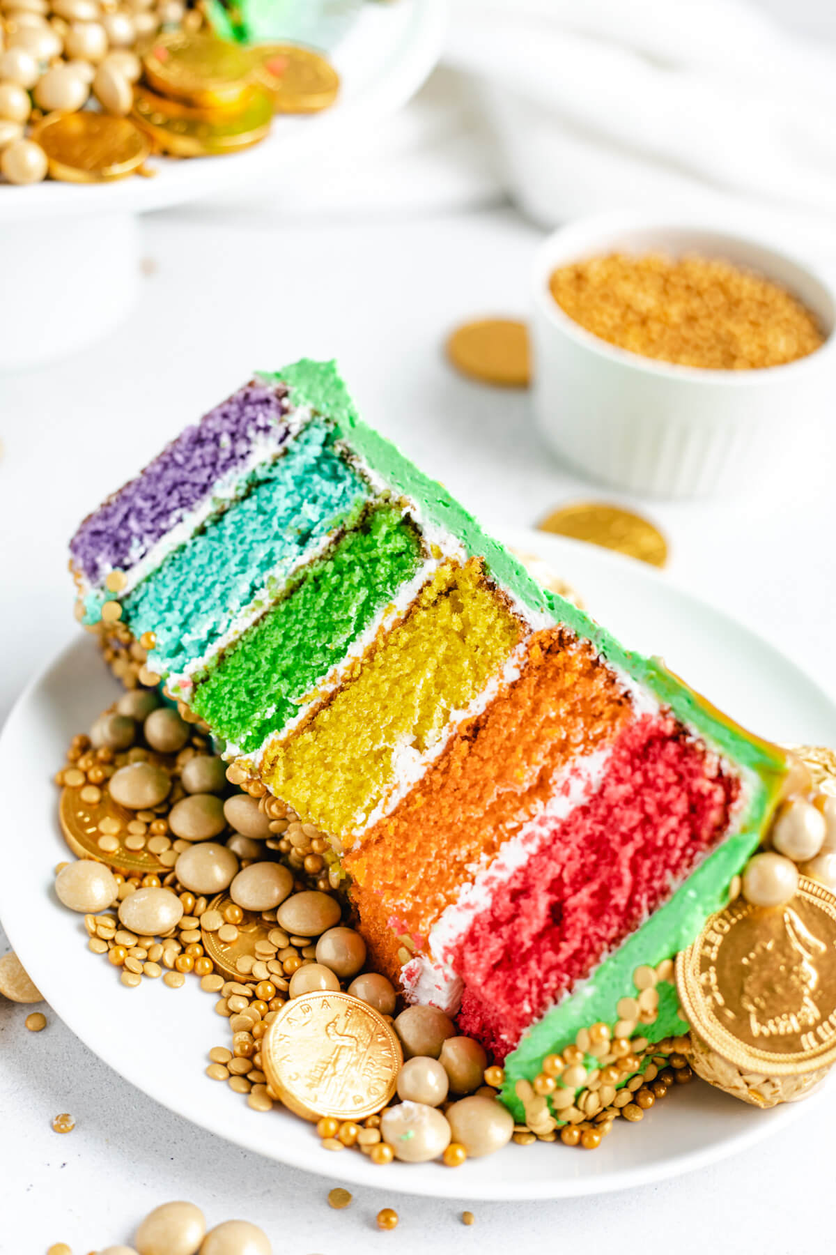 rainbow cake slice with gold sprinkles on a white plate 