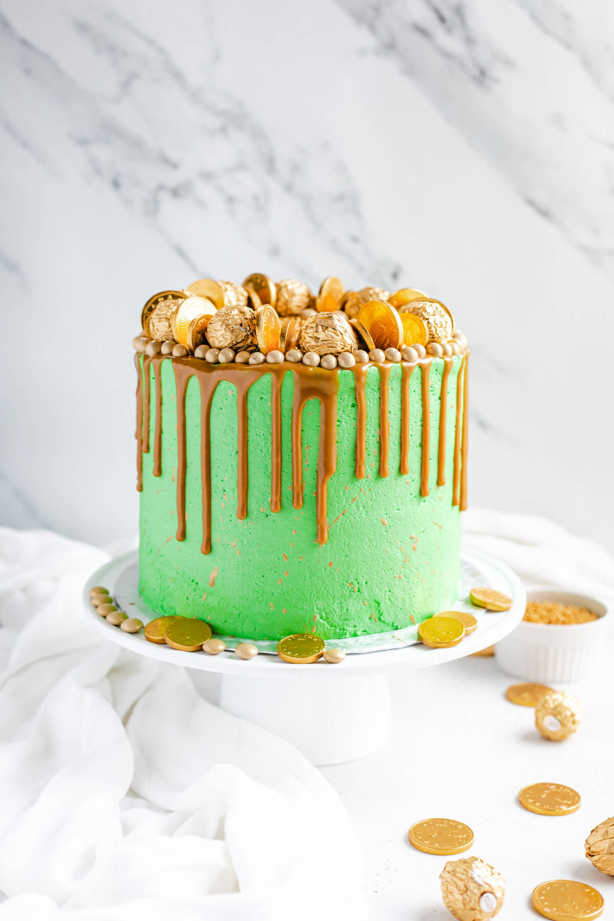 green and gold cake on a white cake stand with gold coins around bottom