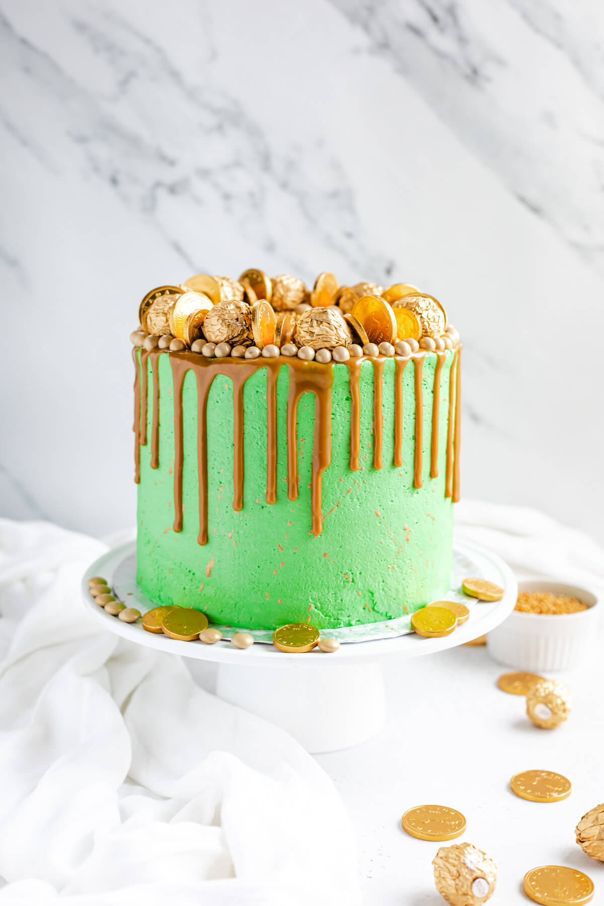 green and gold cake on a white cake stand with gold coins around bottom