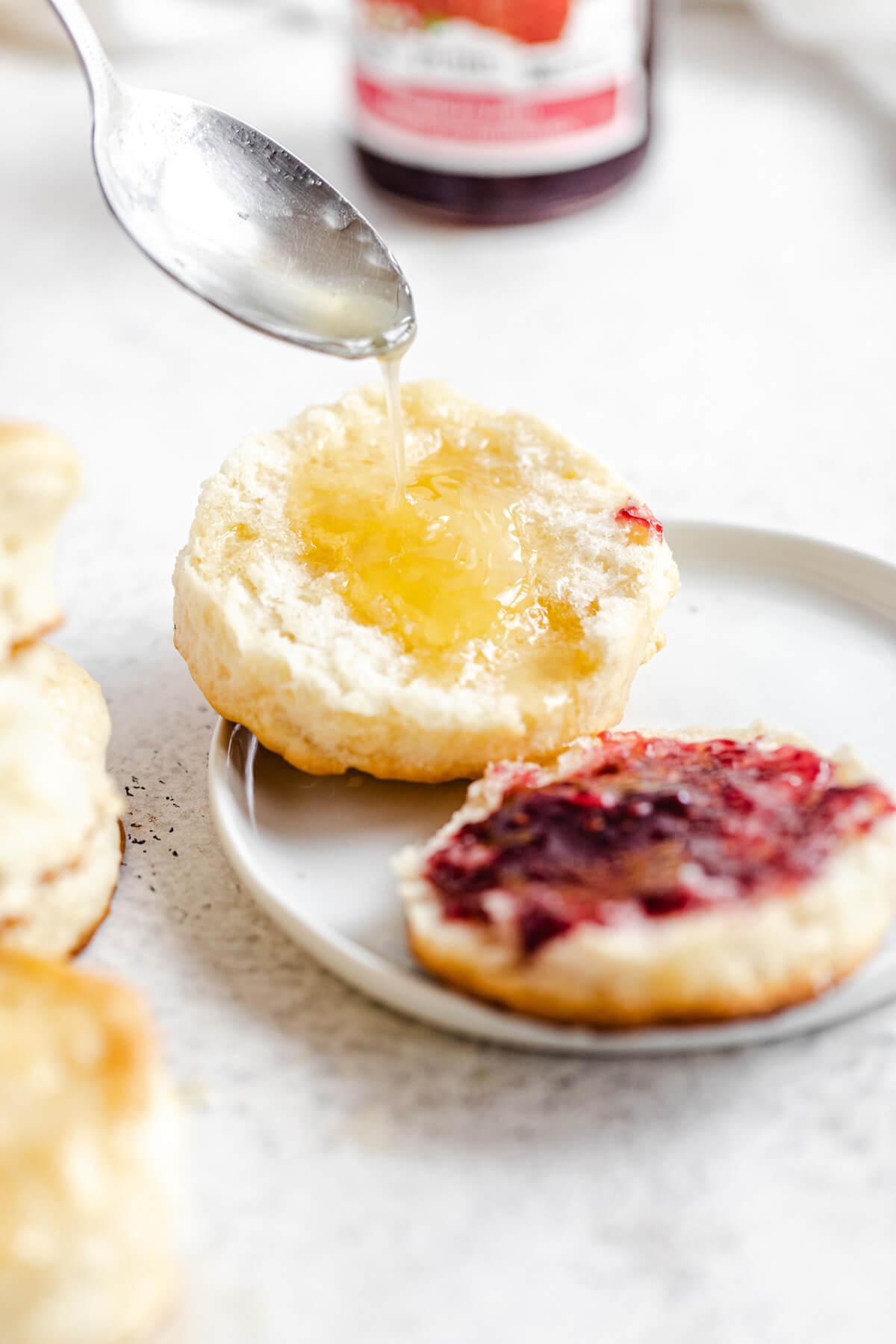 pouring honey butter on one side of a biscuit with jam on the other half