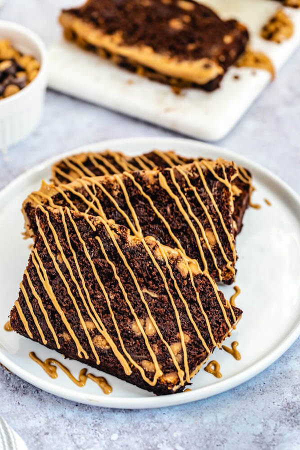 slices of chocolate and peanut butter chip banana bread with peanut butter drizzle on a white plate