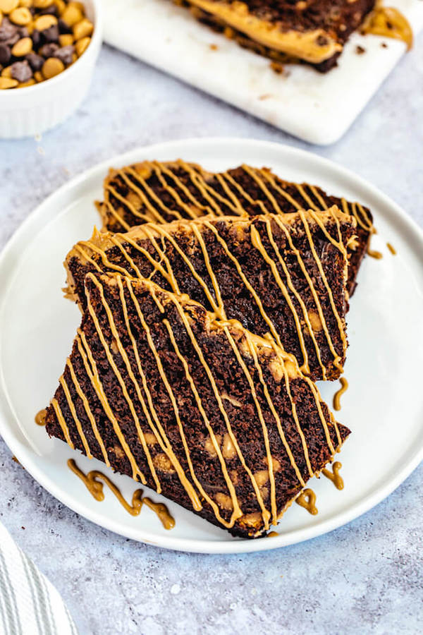 three slices of chocolate banana bread with peanut butter drizzle on a white plate