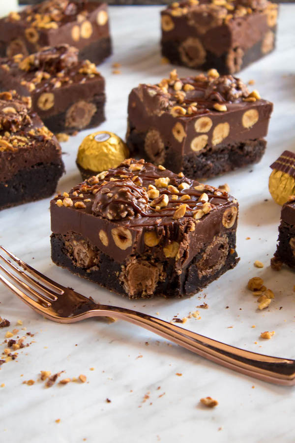 These Ferrero Rocher Fudge Brownies are the ultimate dessert bars! A Ferrero Rocher stuffed fudge brownie, topped with a creamy Nutella Fudge filled and topped with Ferrero Rochers and roasted hazelnuts. Take these bars to another level with a drizzle of silky Nutella Ganache and you’ve got the greatest brownie ever!  