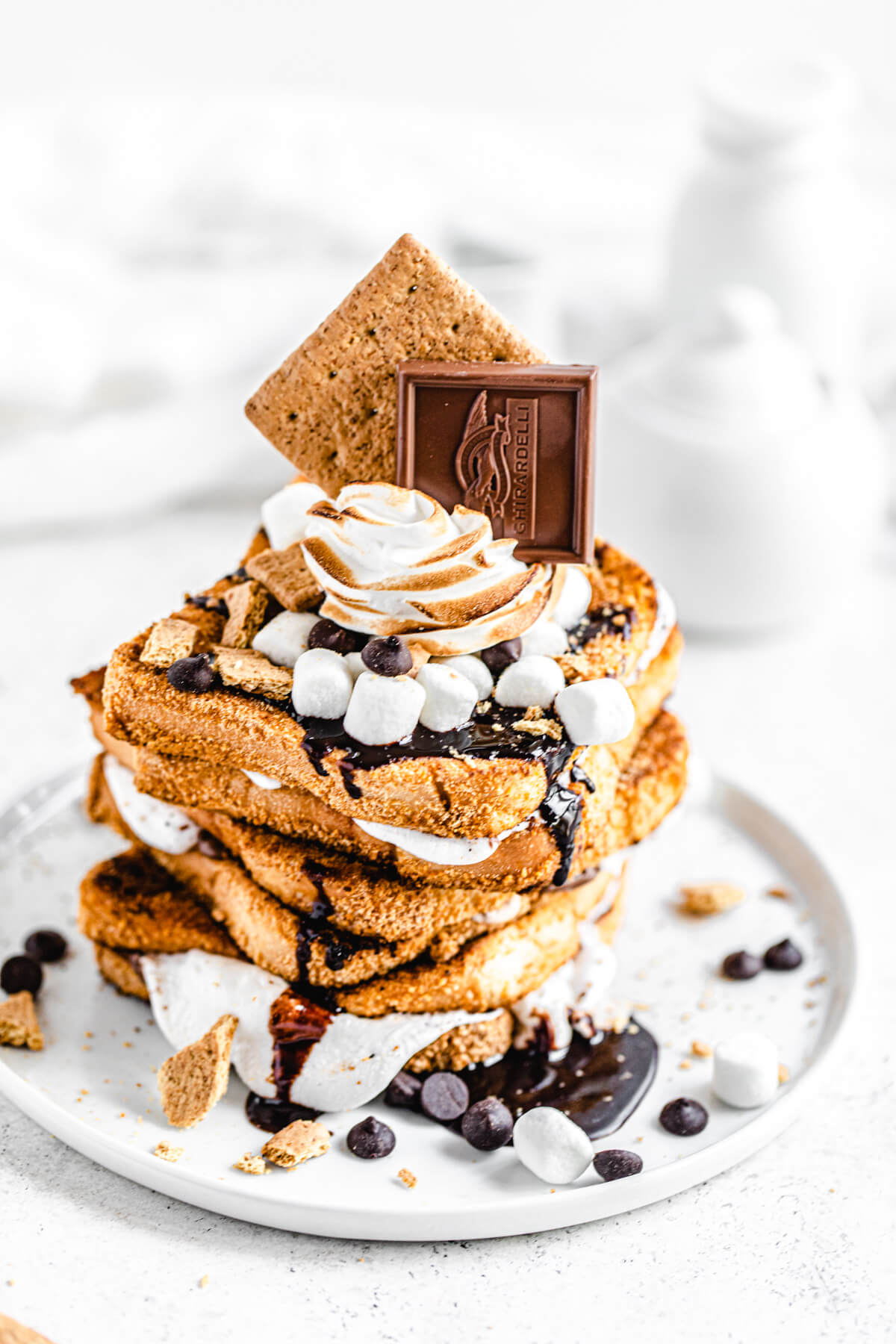 stack of French toast sandwiches topped with marshmallows, toasted meringue, chocolate chips, chocolate sauce and graham crackers on a white plate