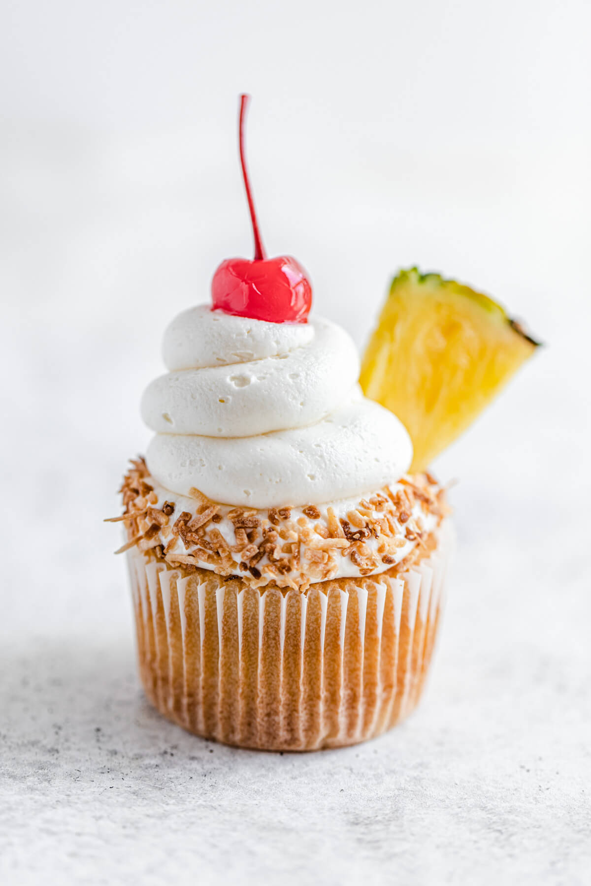 one cupcake dipped in coconut and topped with a cherry and pineapple