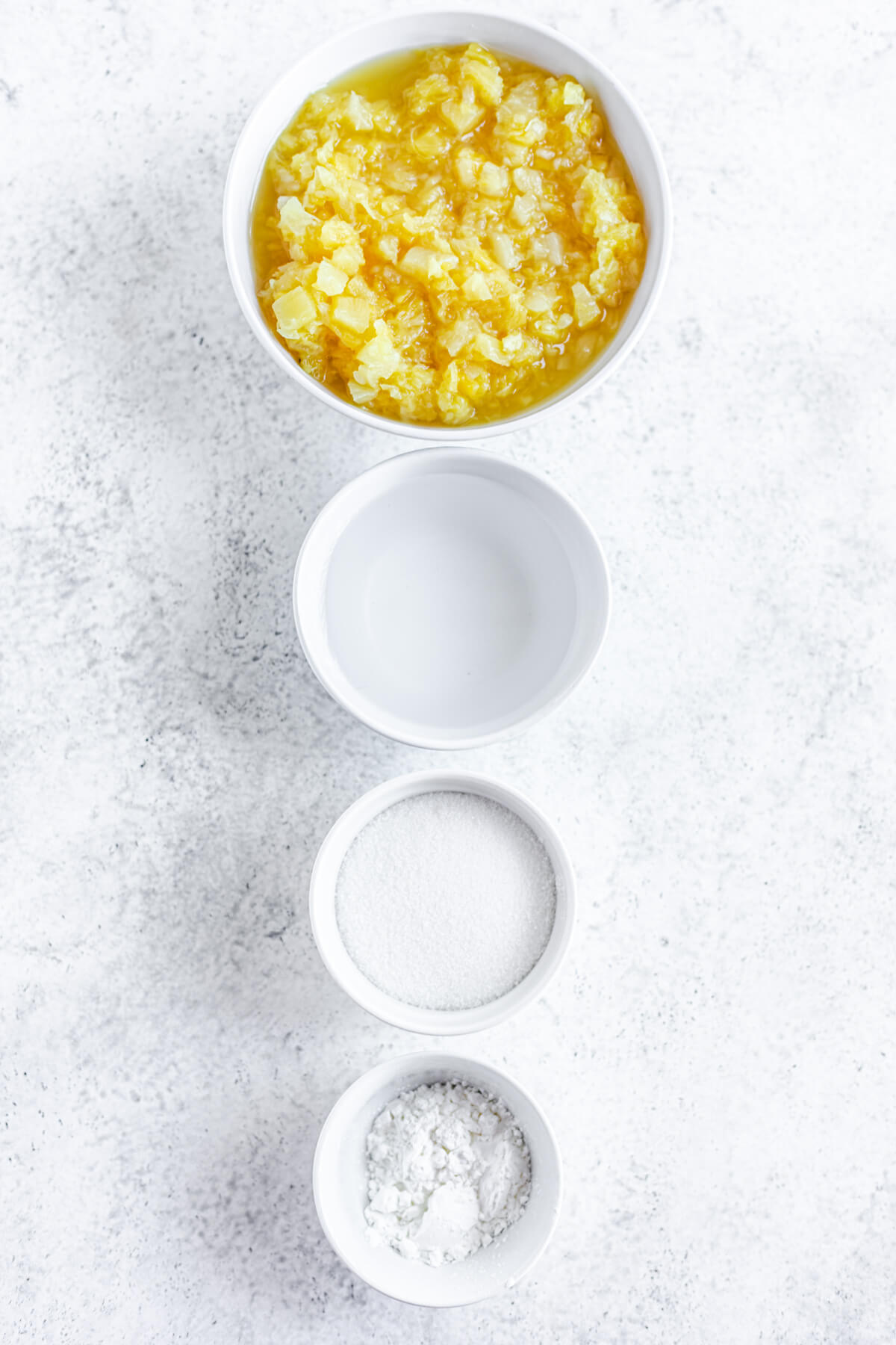 white bowls filled with crushed pineapples, sugar, cornstarch and water lined up in a straight line