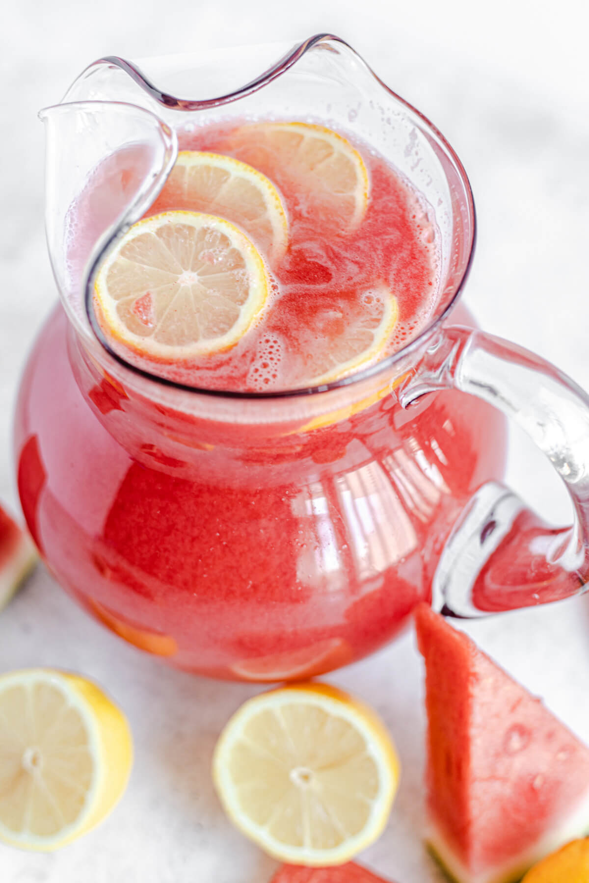 watermelon lemonade in a glass pitcher with lemon slices inside