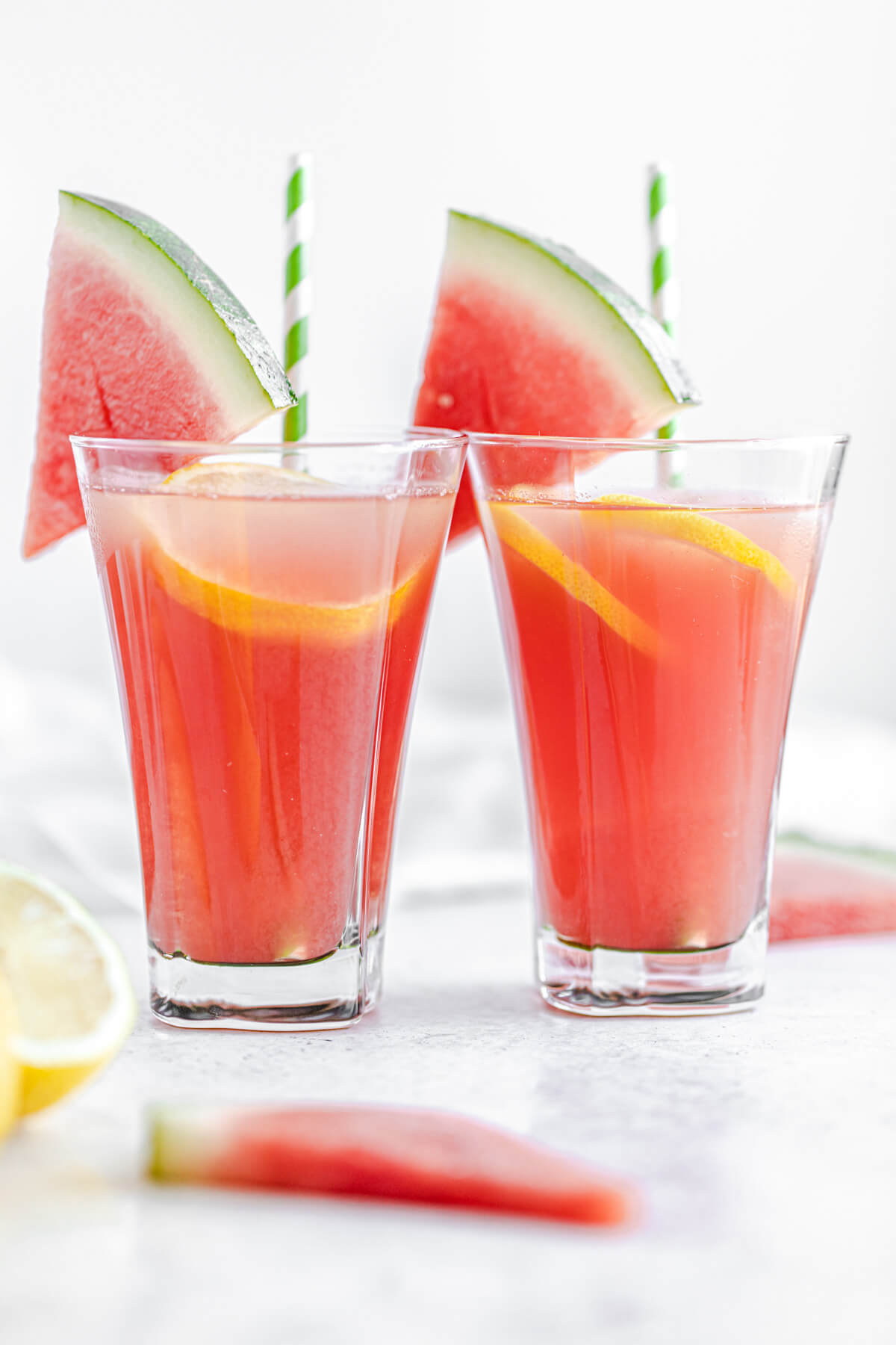 two glasses of lemonade garnished with watermelon wedges and green paper straws