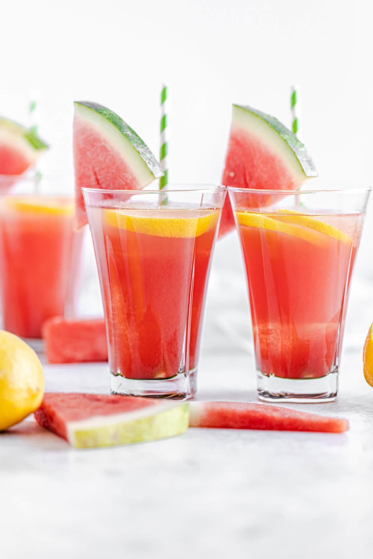 two glasses of watermelon flavoured lemonade with lemons and watermelon in front of them