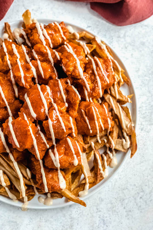 top view of a plate of homemade fries topped with buffalo chicken pieces drizzled with aioli sauce